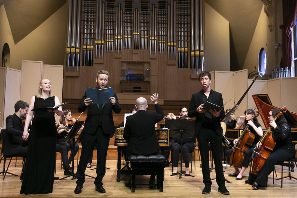 Choral musicians perform alongside a chamebr orchestra on the stage of the Duke's Hall