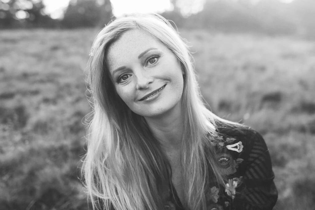 Lucy Crowe smiles for camera, sitting in a field