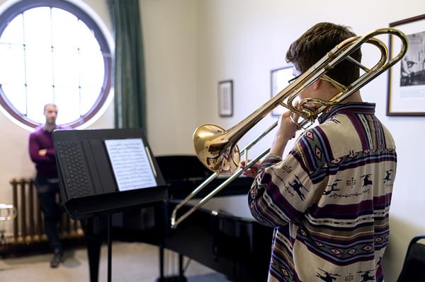 A trumpeter plays music from a lecturn in front of a teacher