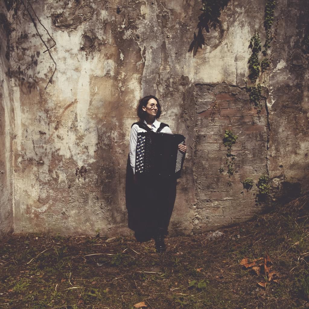 An accordionist stands at a rockface, looking off camera