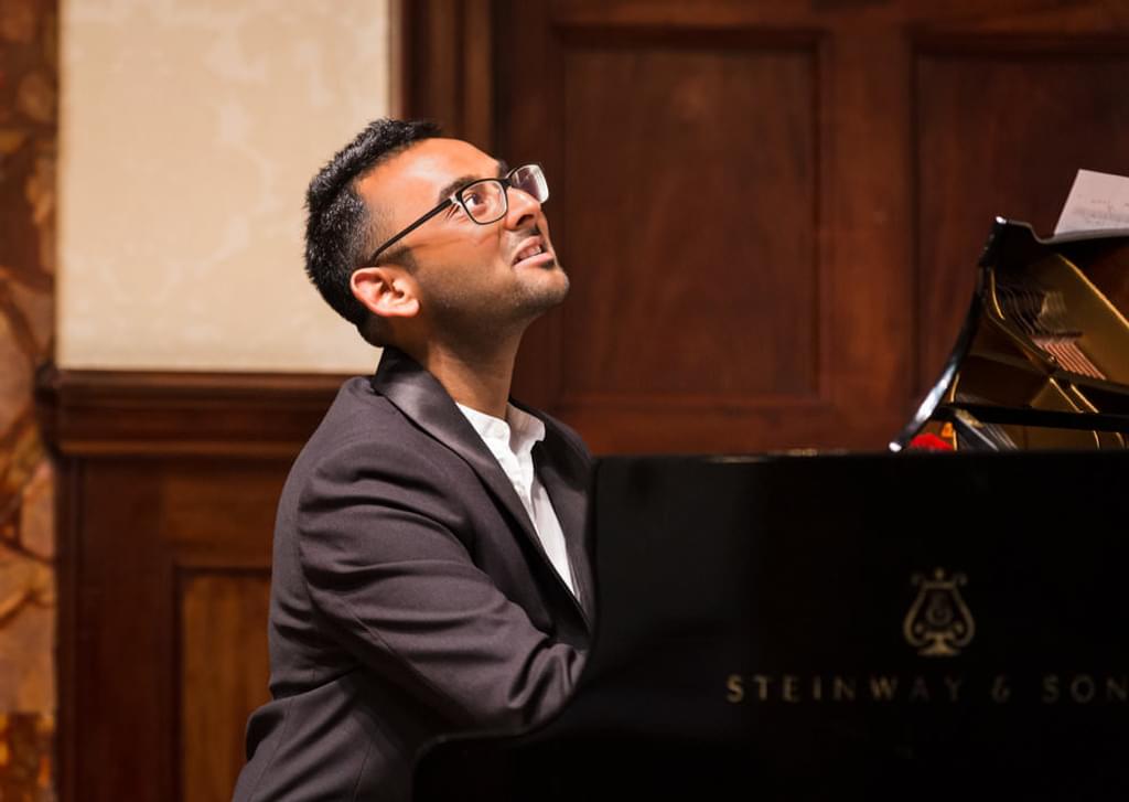 Keval Shah plays a piano, looking upward thoughtfully