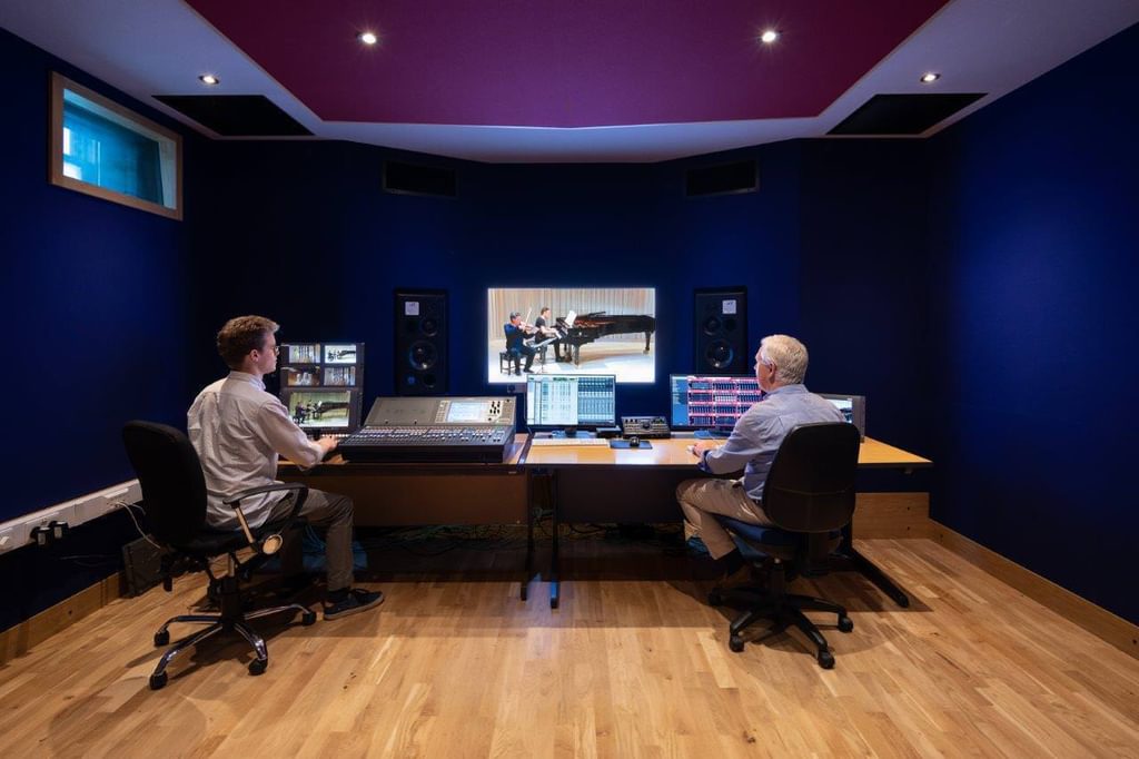 Two engineers sit at the mixing console inside the Academy's live/broadcast room