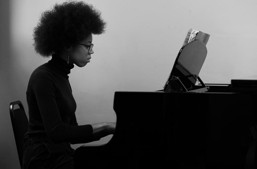 A student sits reading sheet music at a piano