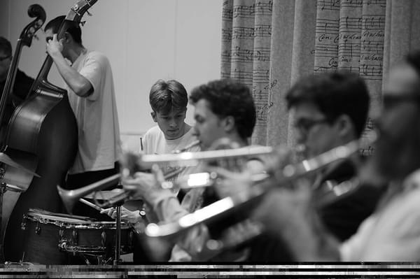 An ensemble of brass players, a drummer and a cellist in rehearsal