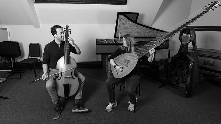 A teacher playing a cello and a student smile during a lesson (black and white)