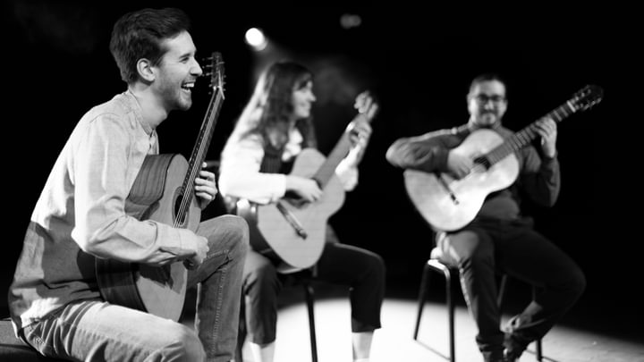 Three guitarists smile on stage in black and white