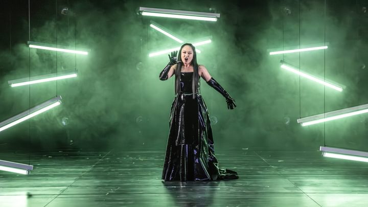 An opera singer mid-performance with a striking green smokey background
