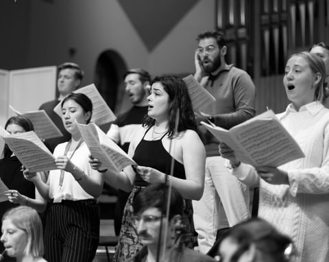 A group of singers perform, facing to the left