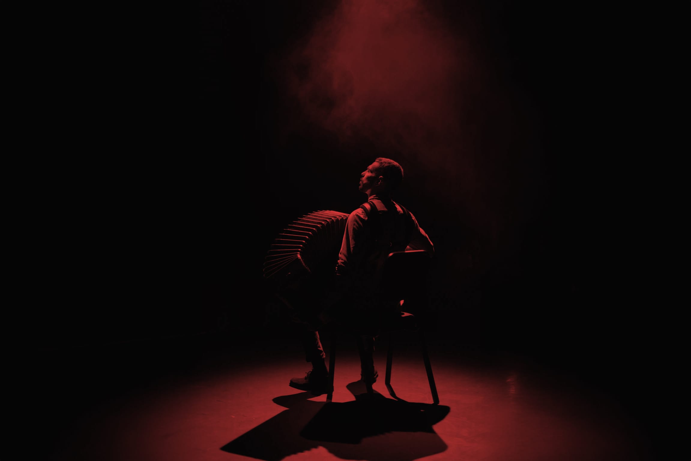 Duotone red and black image of an accordion players looking upwards on stage, covered in a spotlight