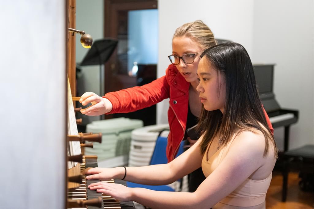 Anna Lapwood at an organ with a Junior Academy student, pointing at a music score and directing the student
