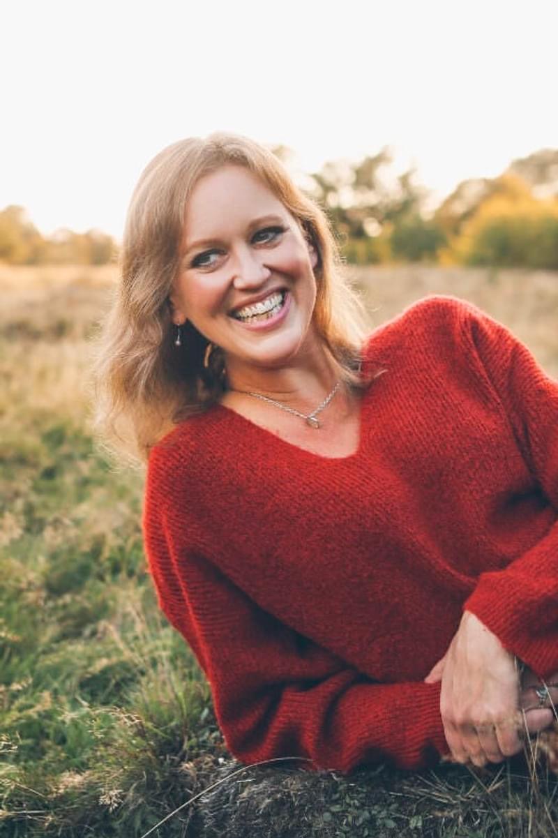 Anna Tilbrook smiles off camera, laying on grass on a sunny day