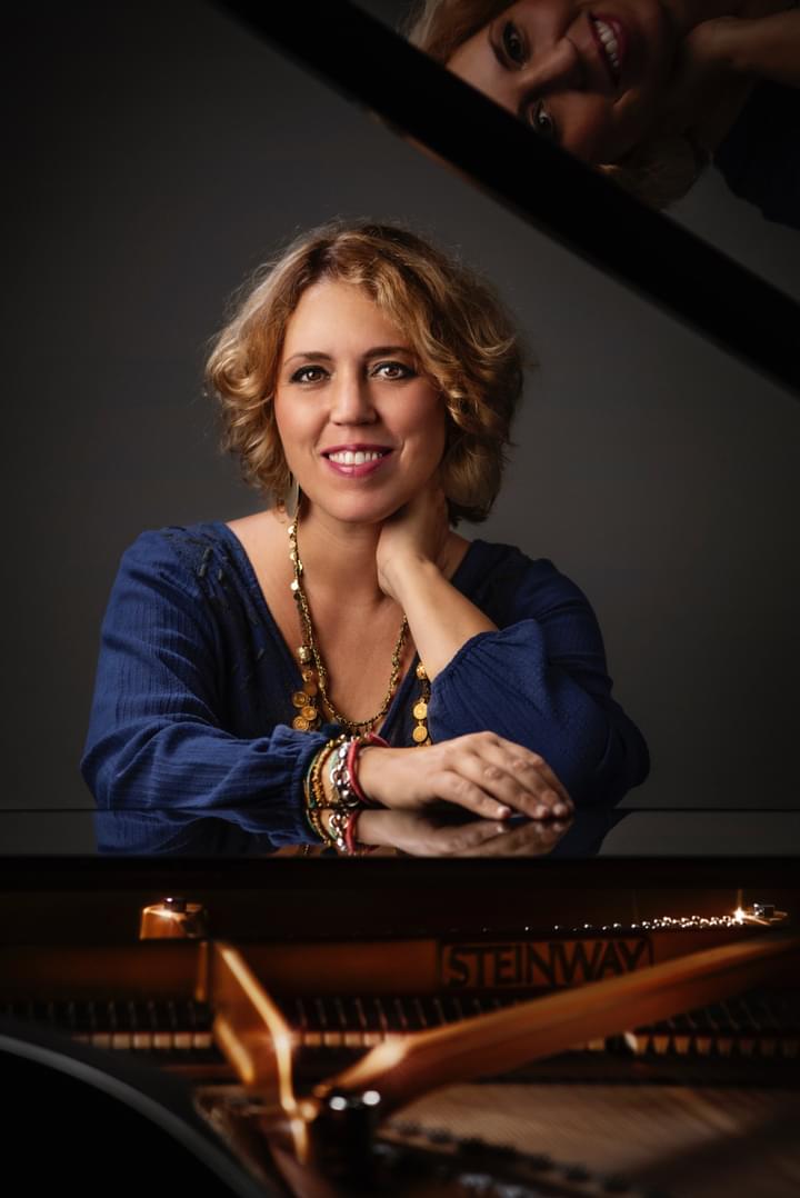 A woman smiles for camera, leaning across the top of a piano