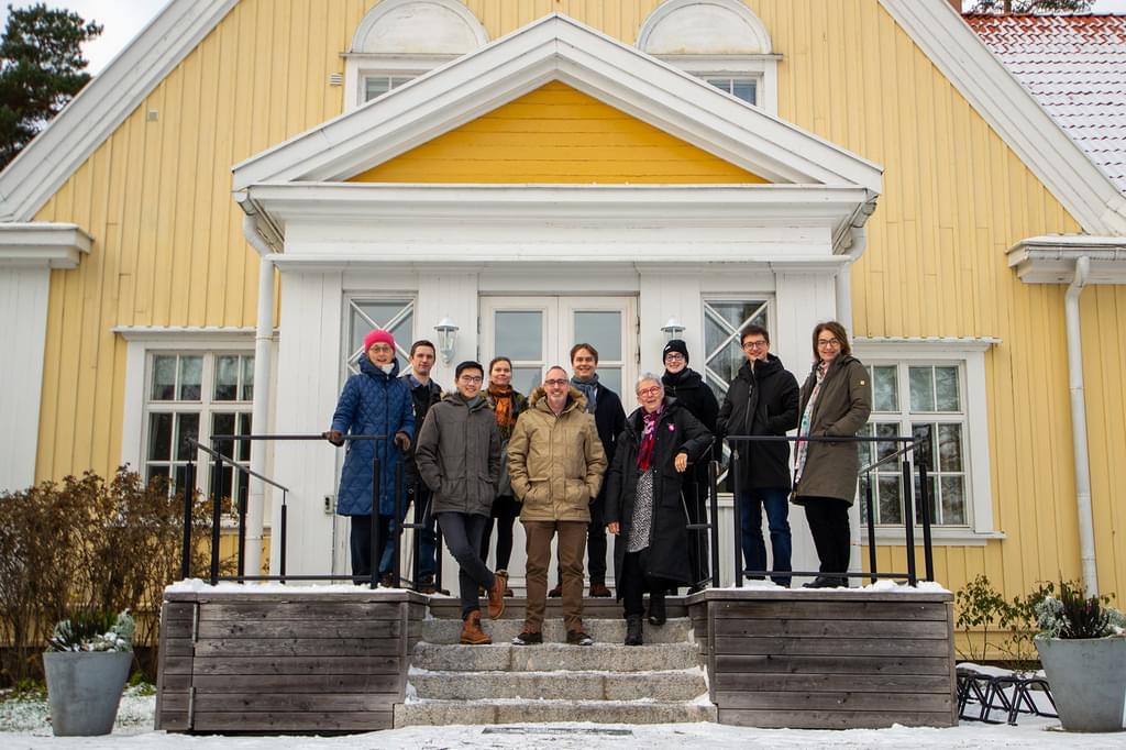 A group of people standing outside on the steps of a yellow building in winter coats