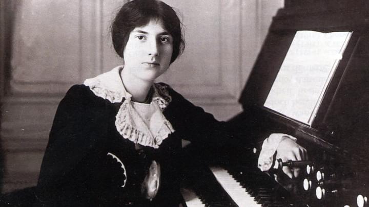A woman sitting at a keyboard with her hair up, wearing a historical black dress with white cuffs and collar.