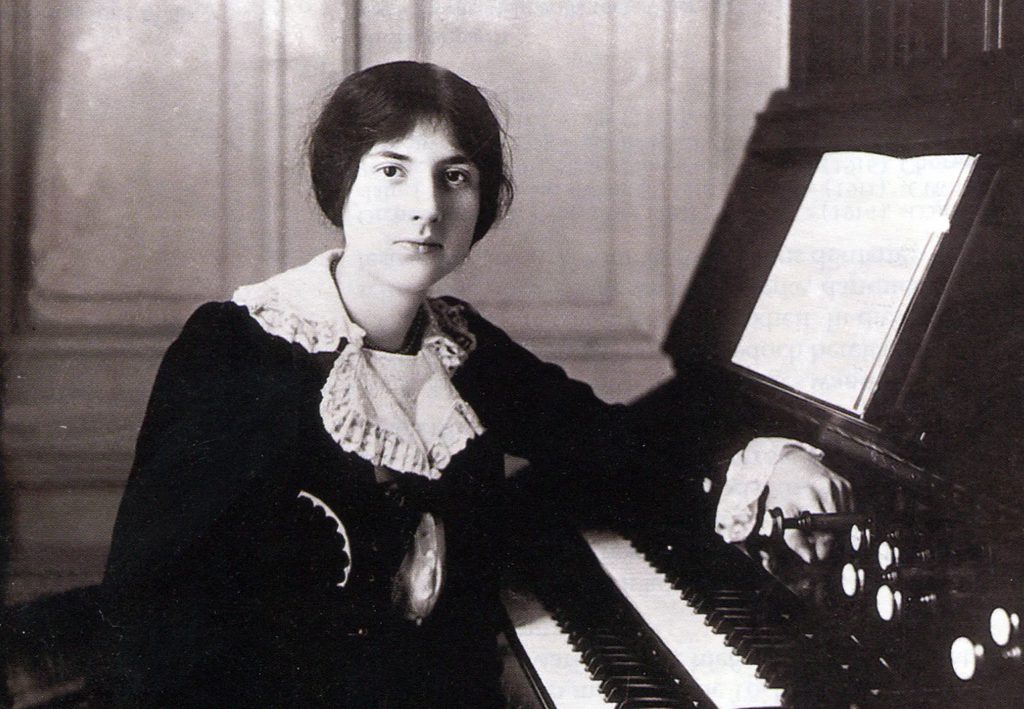 A black and white image of a seated organist in victorian dress leaning against the keys of an organ