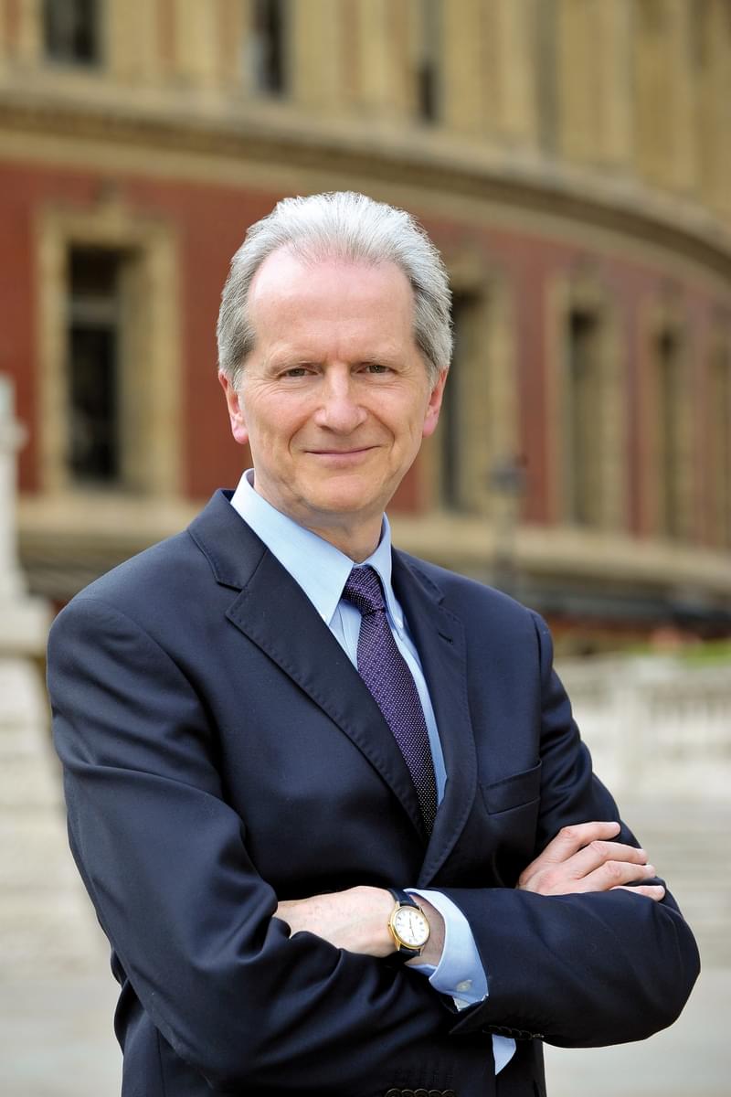 A man in a suit and tie standing with arms crossed in front of a building
