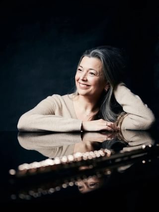 Emily Beynon sits at a table in a dark room, with flute in the foreground