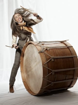Evelyn Glennie strikes a giant tom drum, smiling