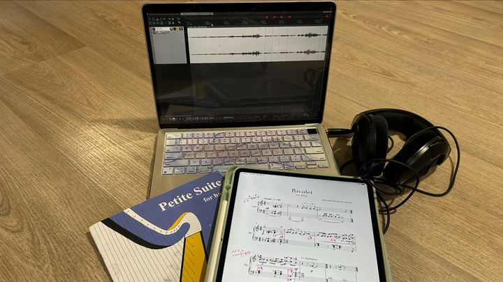 A manuscript, notepad and headphones sit on top of a laptop showing a digital recording