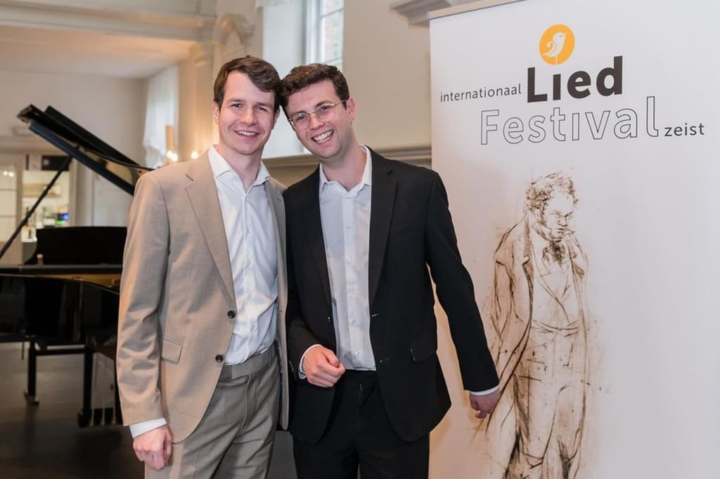 Two men pose for camera at an awards ceremony in front of a popup banner