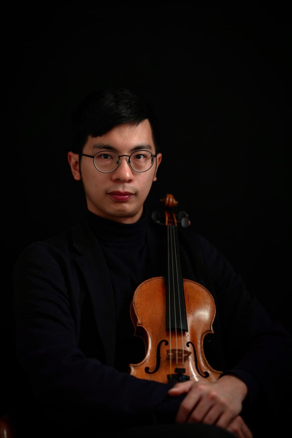 An image of Joe Chu Yu Yang looking into the camera, holding a violin