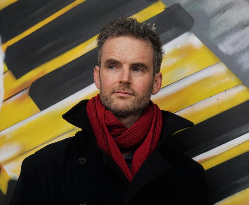 John Reid stands posing for headshot next to an outdoor painted mural at Alexander Palace