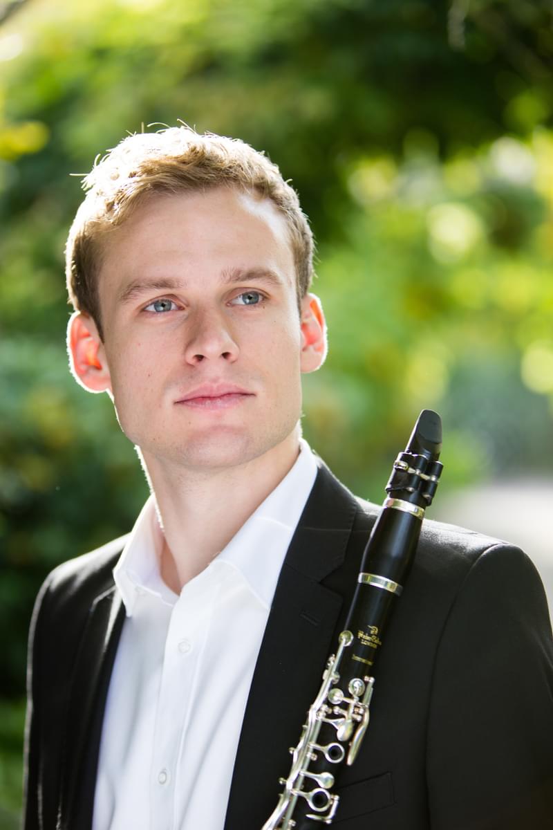 Jordan Black poses for camera holding a clarinet in a green outdoor setting