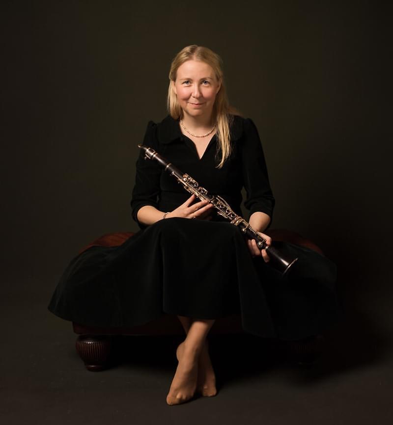 Katherin Spencer sits against a dark background holding a clarinet