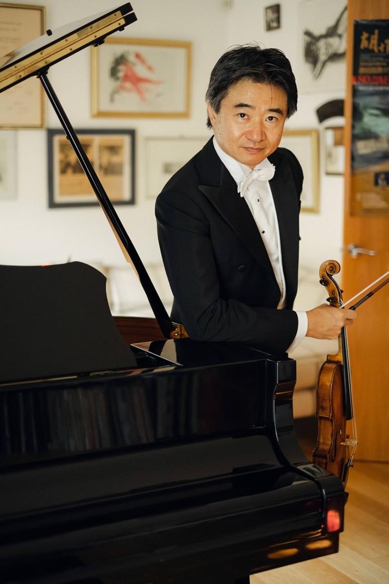 Kun Hu Faces the Camera, Standing at the Side of a Piano