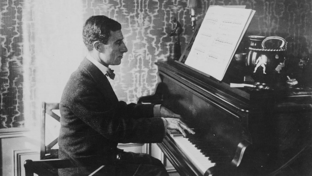Black and white image of Maurice Ravel sitting at a piano