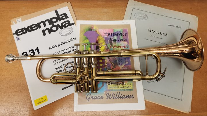 A trumpet lying on top of three musical manuscripts on a desk