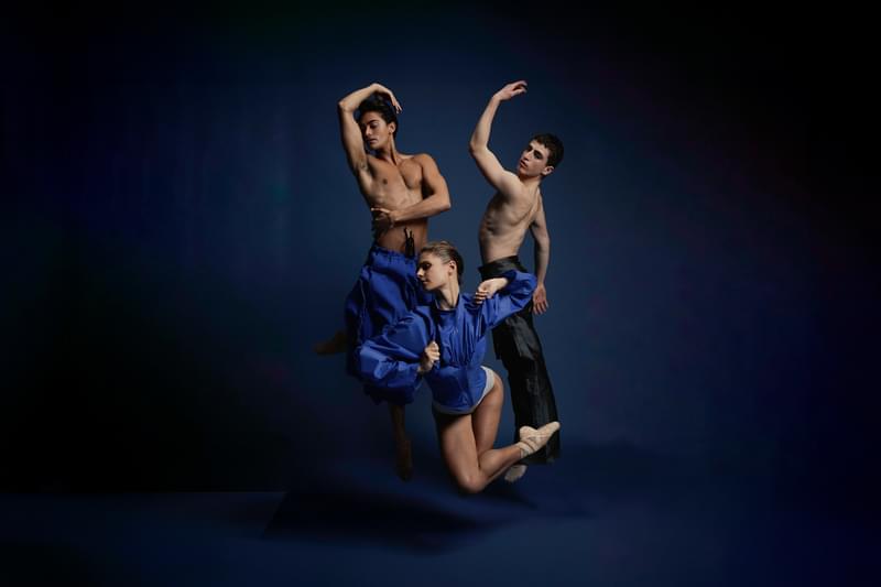 Three dancers pose in striking stances against a blue backgroud