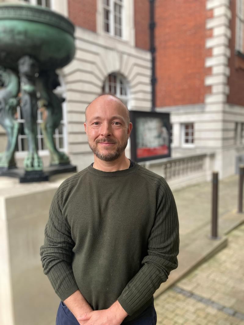 Phil Harmer stands posing for camera outside the entrance of the Academy