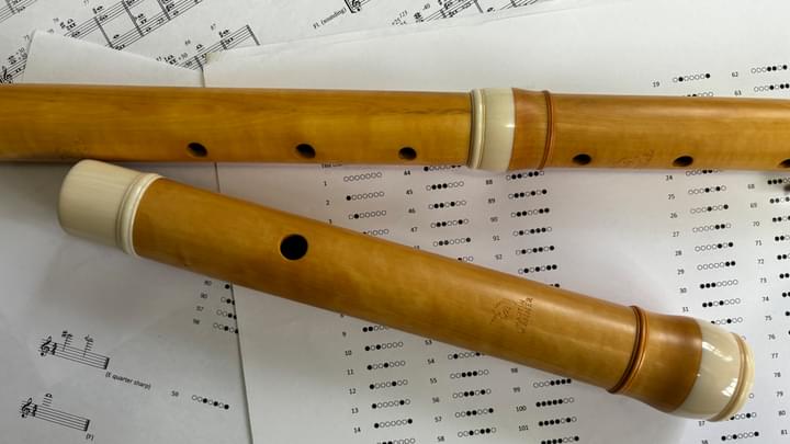 A light wood baroque flute lying on fingering charts and some music scores