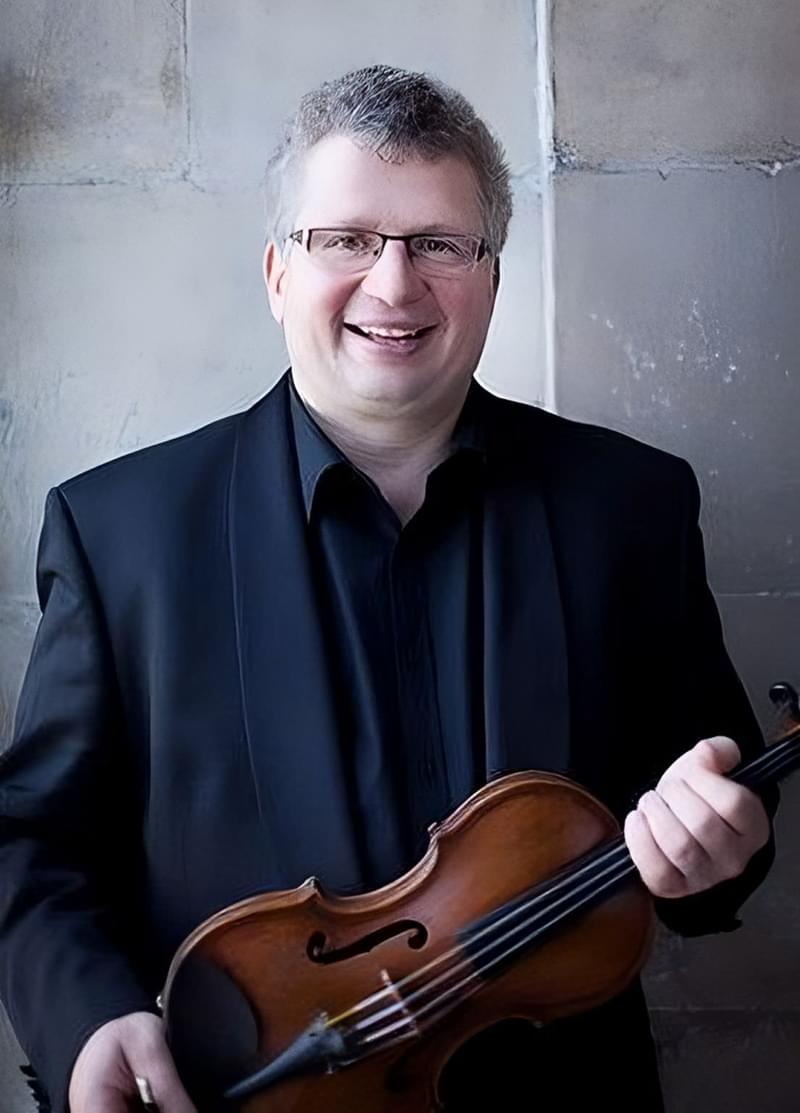 Rafael Todes poses for camera outside, holding a violin at chest with both hands