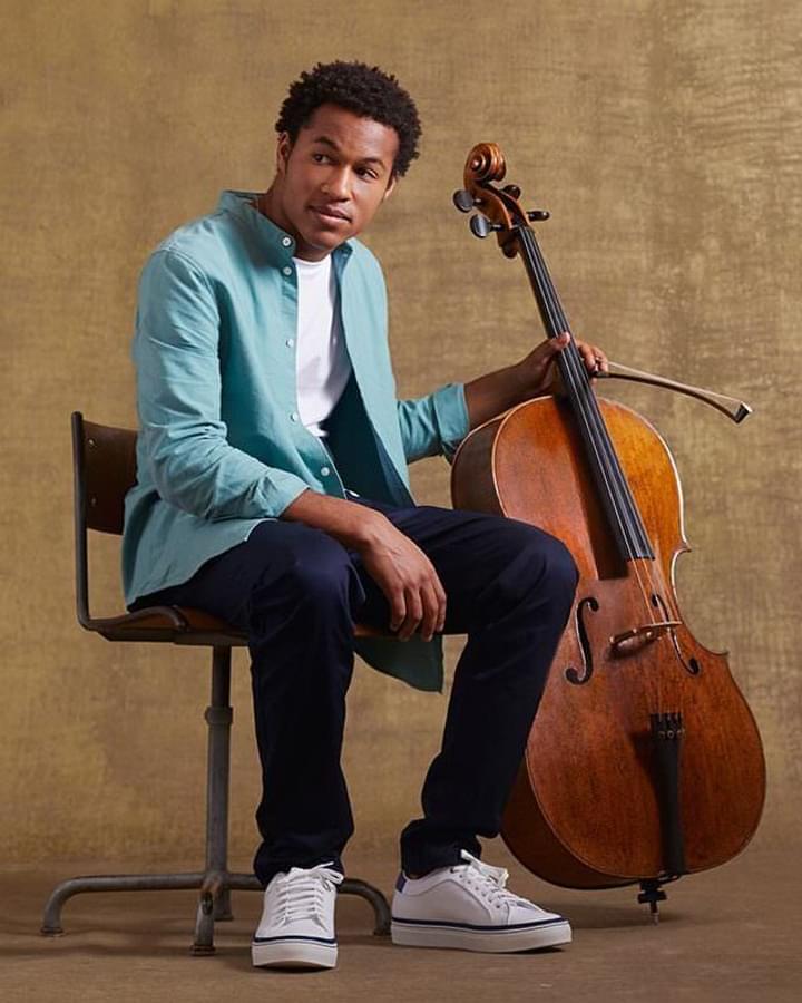 Sheku Kanneh-Mason sits holding his cello, facing camera