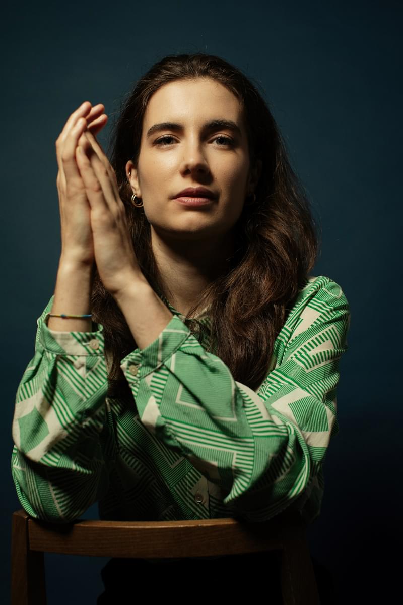 Portrait of Sofia Sacco leaning over the back of a chair, facing camera, clasping hands together