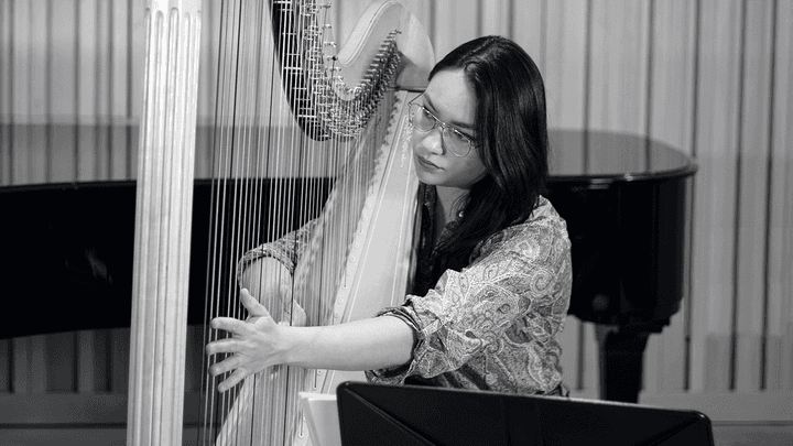 A Harp player plucks strings, glancing through the strings (black and white)