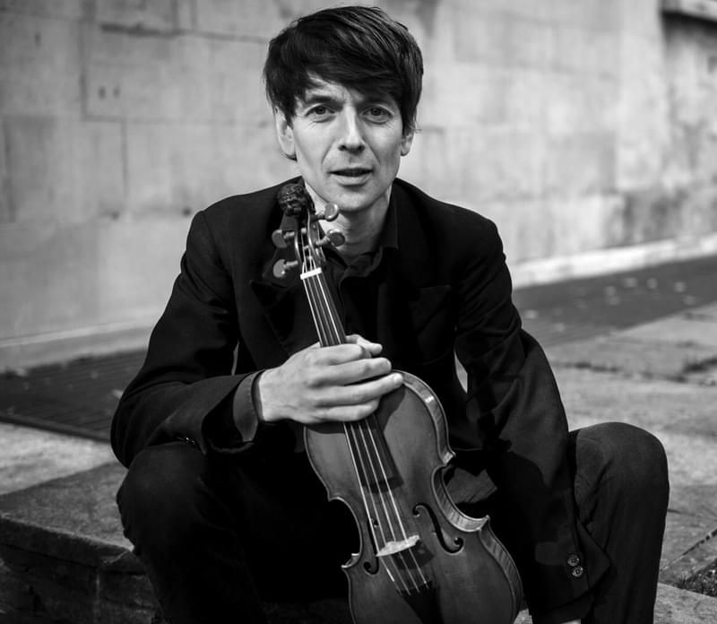 Matthew Truscott sits on the ground holding a violin