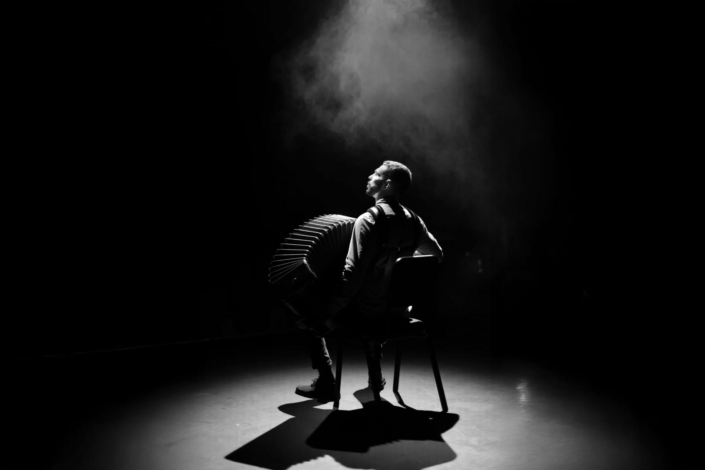 Duotone red and black image of an accordion players looking upwards on stage, covered in a spotlight