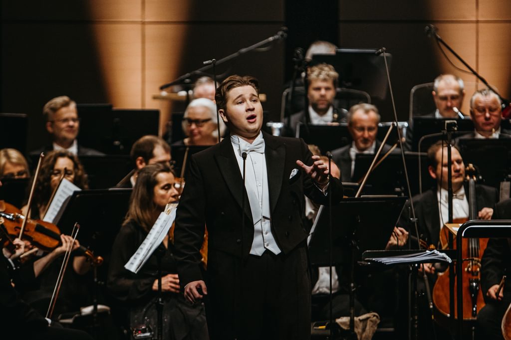 Samuel Stopford pictured singing on stage, with an orchestra behind him