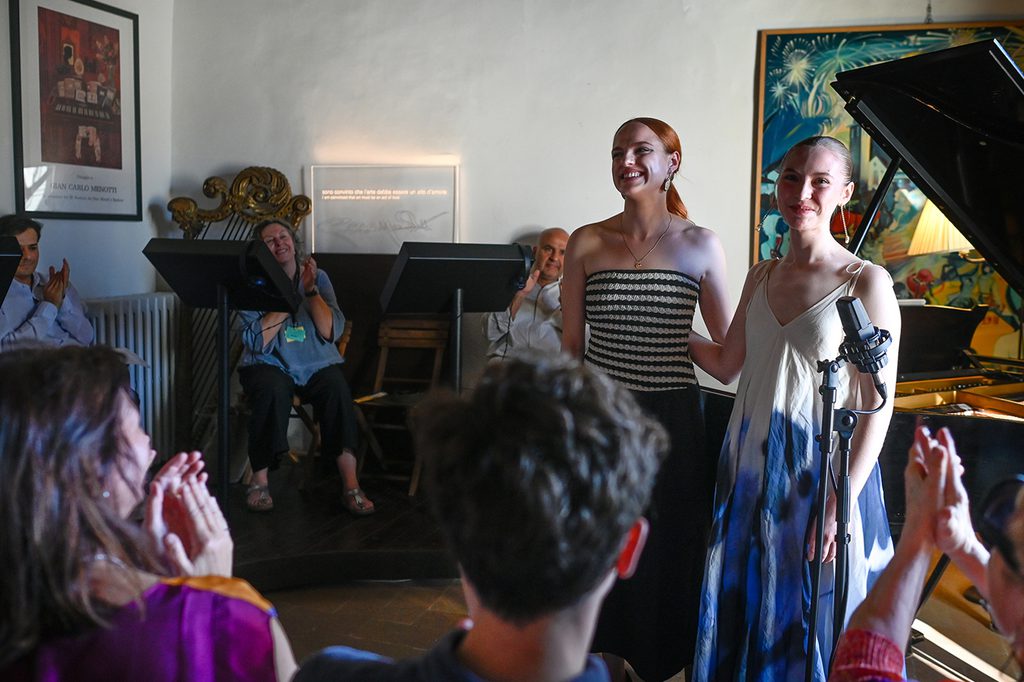 Milda DaunoraitÄ— and Abigail Sinclair standing in front of a piano, receiving an ovation from an audience in a small room