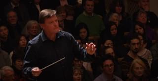 A conductor stands holding baton in front of an audience