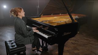 A student sits at a piano with the lid open, playing the keys against a heavy backlight