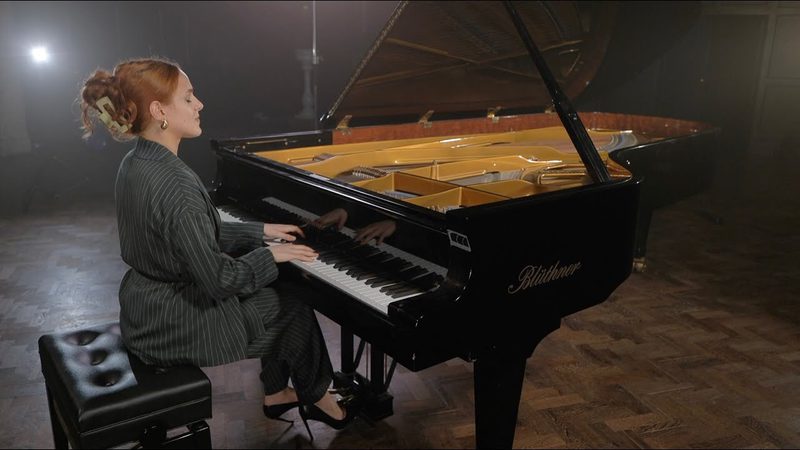 A student sits at a piano with the lid open, playing the keys against a heavy backlight