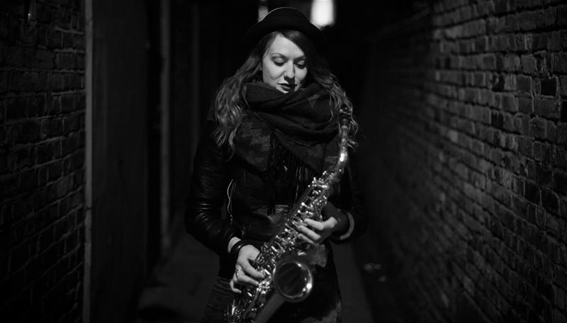 Rachael Cohen holds a saxophone in an alleyway