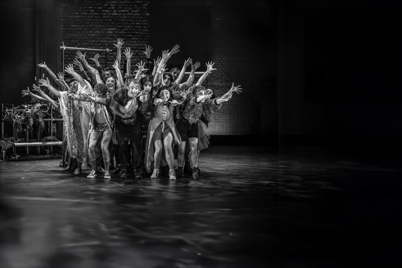 Musical Theatre student strikes a pose, holding their hands forward in a group, black and white