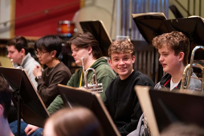 An image of Junior Academy students in rehearsal, with a trumpet player smiling to camera