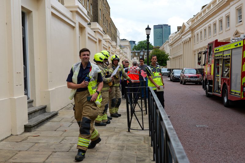 A team of firefighters on a pavement outside a building, looking at documents