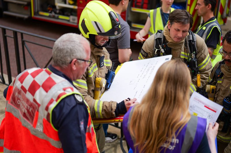 A group of firefighters and people in high-visibility jackets, looking at documents